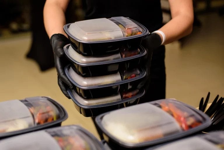 a server wearing black food-safe gloves carrying catered lunch to-go boxes